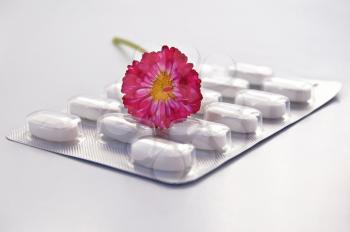 White round pill in a package with daisy isolated on gray background