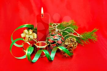 Red burning candle, Christmas tree decorations in the form of a ball, a hand bell with a bow, a drum, cones against red silk