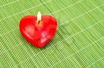 Red candle in the shape of a heart on a green bamboo mat in the upper left corner
