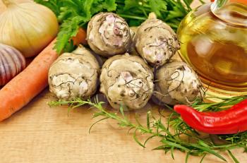 Five tubers of Jerusalem artichoke, garlic, onion, carrot, parsley, a sprig of tarragon, red pepper and a bottle of vegetable oil on a wooden board