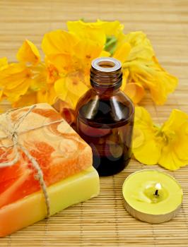 Oil in a bottle, two homemade soaps, nasturtium flowers, yellow candle on a bamboo mat