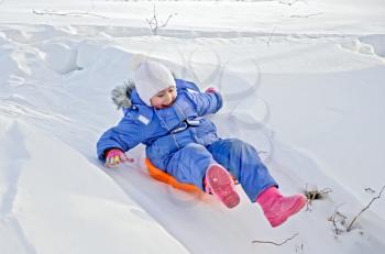 Little girl on a sled sliding down a hill in the snow in winter