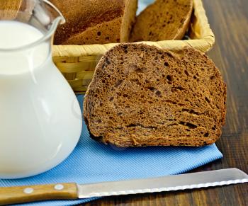 Hunk of homemade rye bread, wicker basket with bread, knife on blue napkin on a wooden board