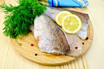 Fillet of codfish on a round plate with lemon and peppercorns, dill, napkin on wooden table