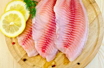 Tilapia fillets with dill, lemon and pepper on a wooden board