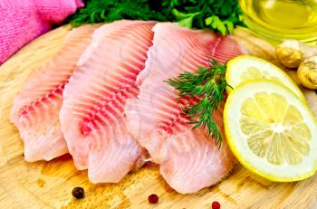 Tilapia fillets with dill, parsley, lemon, a bottle of vegetable oil, ginger, pink cloth, bell pepper on a wooden board
