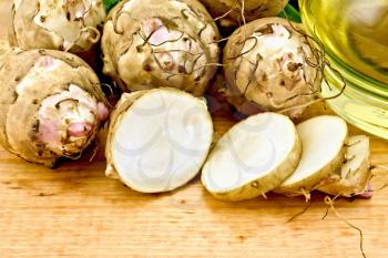 One cut and a few whole tubers of Jerusalem artichoke with a bottle of vegetable oil on a wooden board