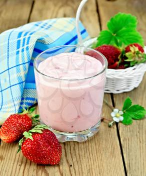 Dairy cocktail in a glass, strawberries in a white wicker basket, flower strawberry with leaves, napkin on a wooden board