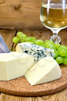 Blue cheese, suluguni, grapes, wine in wineglass, knife on background wooden board