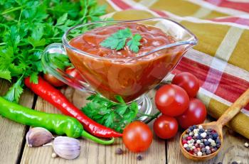 Ketchup in a glass gravy boat, tomatoes, parsley, hot pepper, garlic, napkin on a wooden boards background