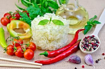 Rice noodles twisted, tomatoes, different pepper, oil in carafe, chopsticks, garlic on a background of sack cloth