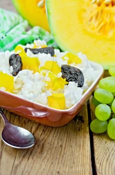 Rice with caramelized pumpkin, prunes in a clay bowl, raw sliced pumpkin, green napkin, grapes on a wooden board