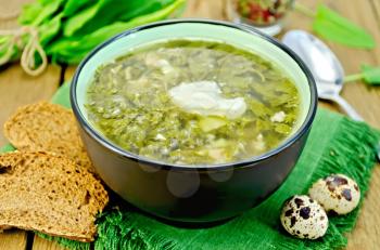 Green soup of sorrel and spinach in a bowl, quail eggs, bread, pepper, spoon on a background of wooden boards