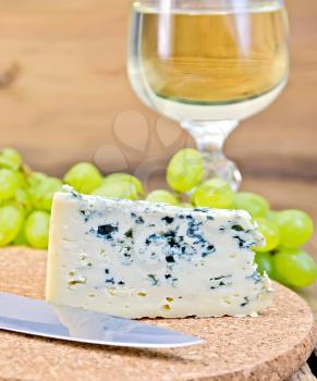Cheese with fungus, grapes, wine glass, knife on background wooden plank