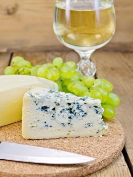 Cheese with fungus, suluguni, grapes, wine glass, a knife on a wooden board