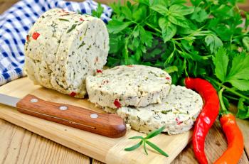 Homemade cheese with herbs, spices and pepper, knife, parsley, rosemary, napkin on wooden board