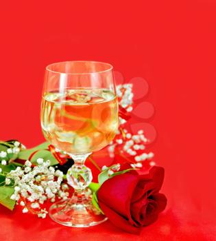 White wine in a glass with a rose on a red fabric