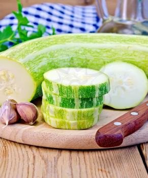 Green zucchini, garlic, a bottle of vegetable oil, parsley, napkin, knife on a wooden board