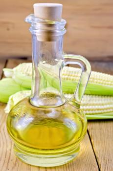 Corn oil in a glass carafe with corn cobs on the background of wooden boards