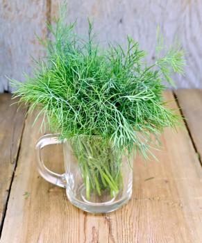 Fresh green dill in a glass mug on a wooden boards background