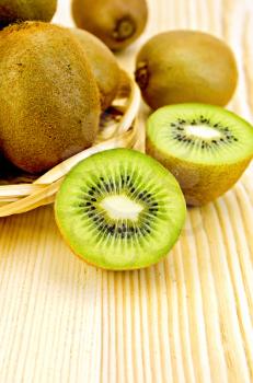 Whole and halves kiwi in a wicker plate and on the background of wooden boards