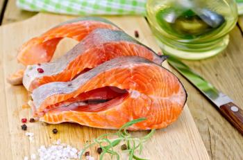 Three pieces of trout with rosemary, coarse salt and pepper, knife, vegetable oil, napkin on the background of wooden boards