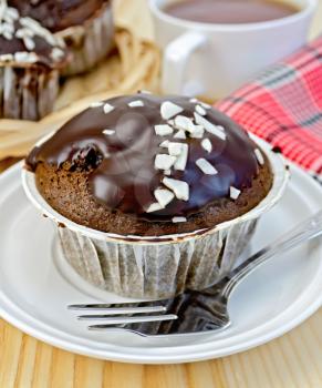 Chocolate cupcake, fork on the plate, red napkin, cup of tea, wicker plate with cupcakes on the background of wooden boards