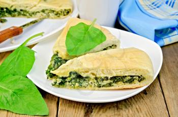 Two pieces of pie with spinach and cheese on a plate, spinach leaves, knife, napkin on the background of wooden boards