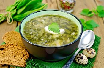 Green soup of sorrel, nettle and spinach in a bowl, spoon, bread, pepper, quail eggs on a wooden board