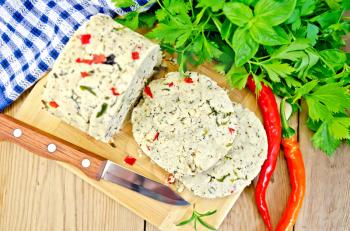 Homemade cheese with herbs, spices and pepper, knife, parsley, rosemary, napkin on the background of wooden boards