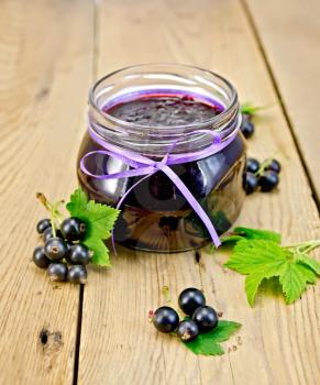 Black currant jam in a glass jar, fresh black currant berries with leaves on a wooden board