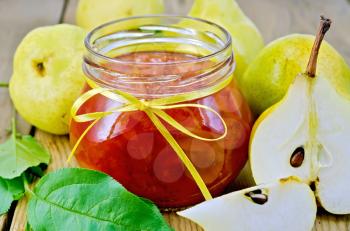 Pear jam in a glass jar, fresh pears, twigs with leaves on the background of wooden boards