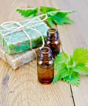 Oil in bottles, two bars of homemade soap, nettle on the background of wooden boards