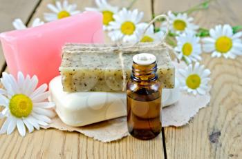 Oil in a bottle, homemade soap on a piece of paper, daisy flowers on a background of wooden boards