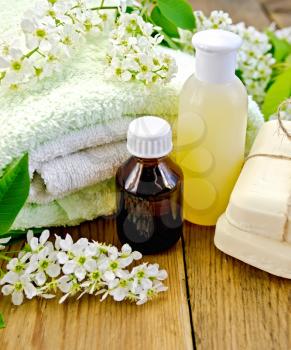 Oil and lotion bottles, soap, flowers bird cherry, a towel on the background of wooden boards