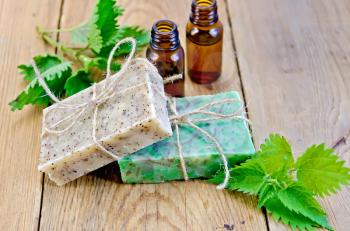 Oil in bottles, two bars of homemade soap with twine, nettle on the background of wooden boards