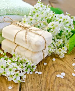 Two pieces of white soap, flowers, bird cherry, a towel on the background of wooden boards