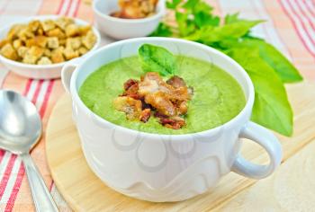Green soup puree in a white bowl with grilled meat and spinach leaves, spoon on a wooden board on the background fabric