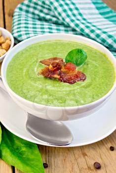 Green soup puree in a white bowl with spinach and grilled meat, napkin, crackers, spoon on a wooden boards background
