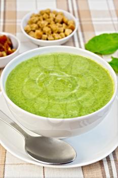 Cream soup green from spinach in a white cup and saucer, spoon, spinach leaves, croutons on fabric background