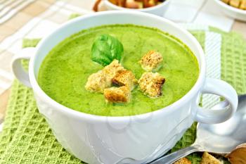 Green soup puree in a white bowl with croutons and spinach leaves on a napkin on the background fabric
