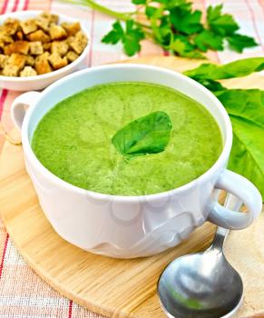 Green soup puree in a bowl with green leaf spinach, spoon on the board, crunches on fabric background