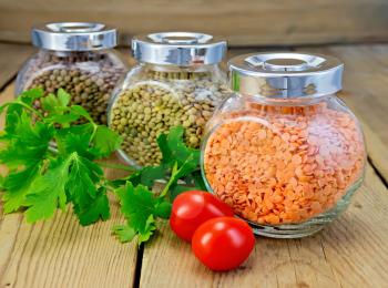 Lentils red, green, brown in glass jars, parsley, tomatoes on a wooden boards background
