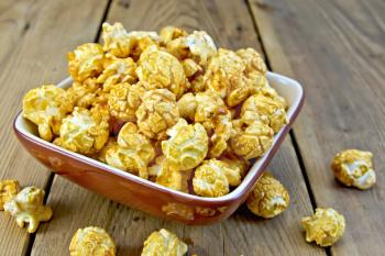Caramel popcorn in a clay bowl on a wooden boards background