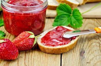 Bread with strawberry jam, a jar of jam, knife, strawberries on a wooden boards background