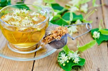 Metal sieve with dried flowers of lime, fresh flowers linden, tea in glass cup on the background of wooden boards