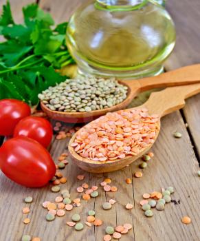 Red and green lentils in a wooden spoon, tomatoes, parsley, vegetable oil in a carafe on the background of wooden boards