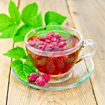 Tea with raspberries in a glass cup, raspberry leaves on the background of wooden boards