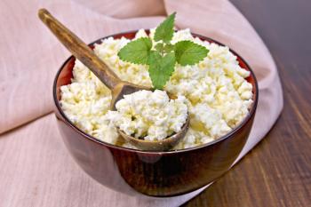 Cottage cheese in a wooden bowl with a spoon on a napkin and mint on a wooden boards background