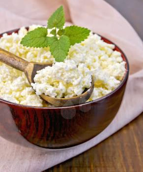 Cottage cheese in a wooden bowl with a spoon on a napkin and mint on a wooden boards background